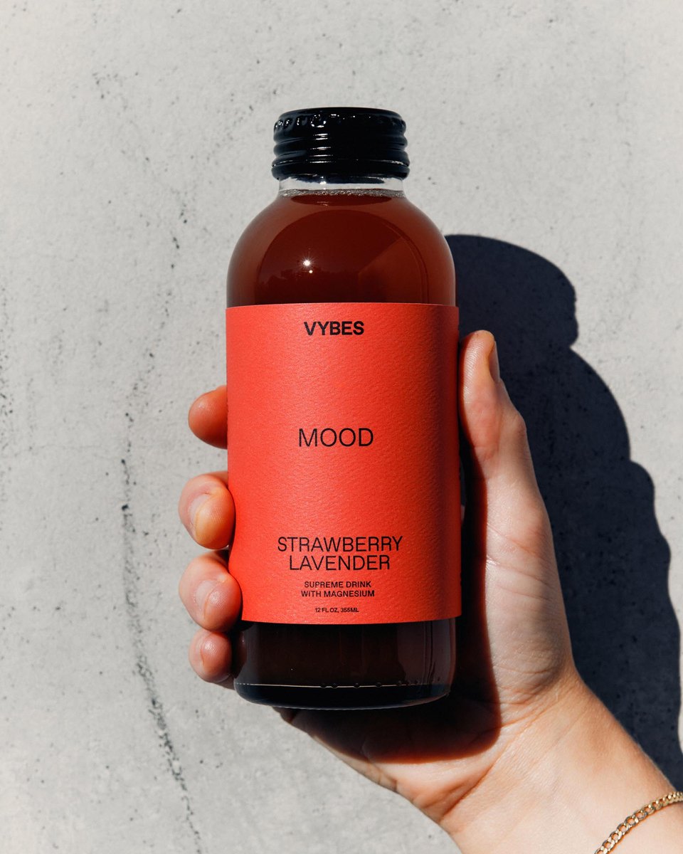 A hand holding a VYBES Strawberry Lavender Mood drink in the sun